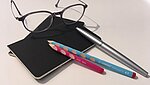 Brille mit Notizbuch und Stiften als Forschungssymbol