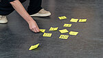 Das Bild zeigt eine Themensammlung mit Post-its auf dem Boden und die Hände einer Person, die diese in eine Ordnung bringt.
