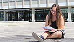 sitzende Studentin vor dem Hauptgebäude sieht sich Unterlagen an