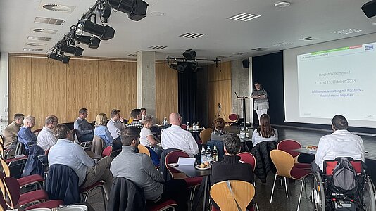 Ca. 25 Personen sitzen um Tische gruppiert im Litcafe. Auf der Bühne trägt Dr. Petra Schneidewind vor.