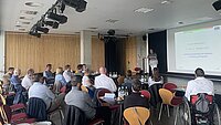 Ca. 25 Personen sitzen um Tische gruppiert im Litcafe. Auf der Bühne trägt Dr. Petra Schneidewind vor.
