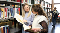 Zwei Studierende in der Bibliothek mit B&uuml;chern in der Hand.