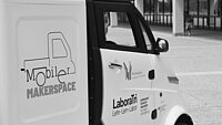 Kleines weißes Auto in der Seitenansicht mit Aufschift: Mobiler Makerspace