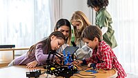 Kinder arbeiten gemeinsam an einem Tisch an Robotern