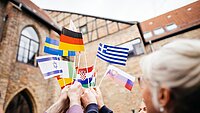 Hochschulvertreter:innen halten Fähnchen mit den Flaggen verschiedener europäischer Länder in die Luft