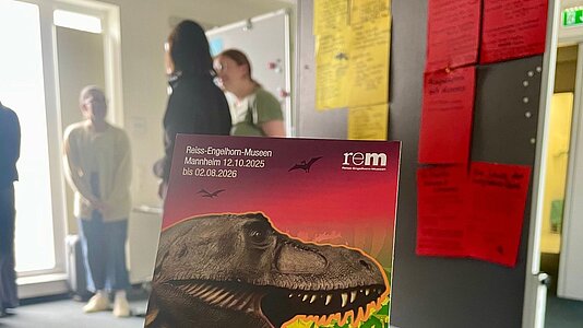 Flyer der Ausstellung "Saurier", im Hintergrund Studierende