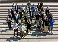 Die Teilnehmer*innen der Veranstaltung stehen auf einer Treppe und blicken in die Kamera