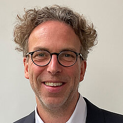 Herr Sven Wippermann hat braune Locken. Er tr&auml;gt ein schwarzes Jacket und ein wei&szlig;es Hemd. 