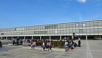 Studierende sitzen auf dem sonnigen Campusgelände vor dem Gebäude 1 und g