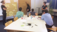 Auf dem Bild sind Studierende zu sehen, die den Design Thinking Workshop 2018 belegt haben. Sie arbeiten in der Kleingruppe an einer Metaplantafel.