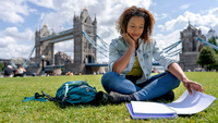 Studierende sitzt vor der Tower Bridge in London und lernt.
