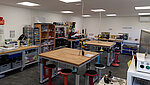 Ein Foto des Makerspaces mit Tischen im Zentrum und an der Wand befindlichen Geräten wie 3D-Drucker, Stickmaschien, Lasercutter.