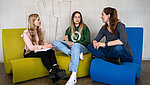 drei Studentinnen sitzen auf den bunten Sitzhockern des Lichtgangs der Pädagogischen Hochschule Ludwigsburg.